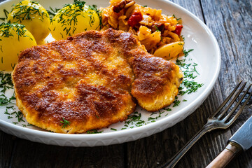 Breaded fried pork chop with boiled potatoes and cabbage on wooden table
