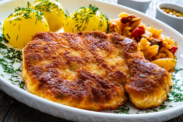 Breaded fried pork chop with boiled potatoes and cabbage on wooden table
