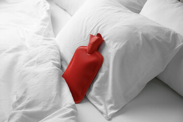Rubber hot water bottle near soft pillow on bed