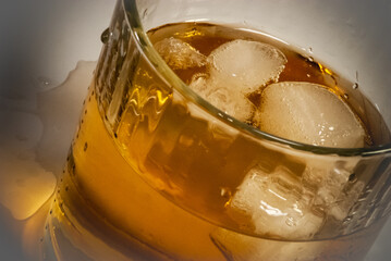 A spilled messy alcohol highball drink with ice cubes in cheap glass tumbler.