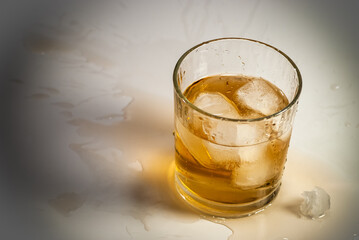A spilled messy alcohol highball drink with ice cubes in cheap glass tumbler.