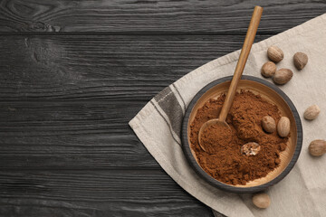 Nutmeg powder and seeds on black wooden table, top view. Space for text