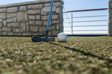 Golf on a cruise ship. Putting a golf ball on artificial turf. Golf putter, putting green, no brand golf ball, blurred background.