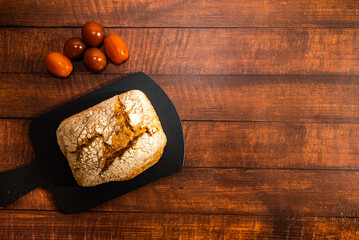 Freshly baked whole wheat bread with red cherry tomatoes. Dark wooden table background