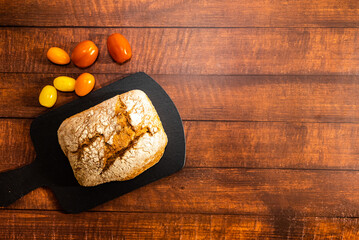 Freshly baked wholemeal bread with cherry tomatoes of different colors. Dark wooden table background