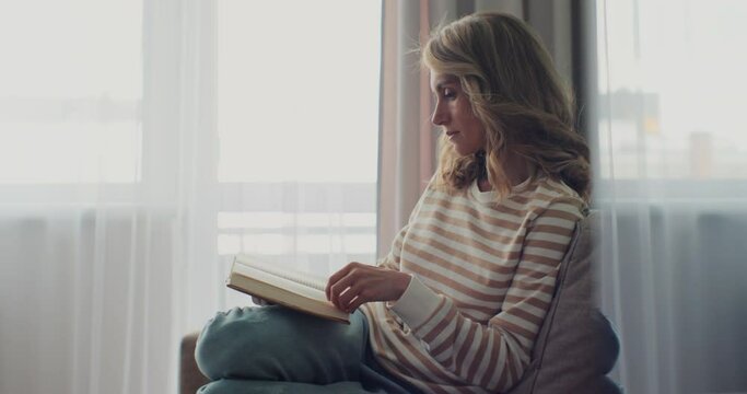 Attractive woman reading book while sitting on a sofa at home. Feels calm and comfortable.