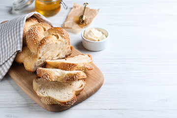 Cut freshly baked braided bread and butter on white wooden table, space for text. Traditional...