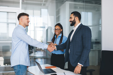 Multiracial male employees in smart casual clothing doing handshake during business meeting in...