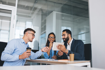 Professional male and female employees discussing website project during working process in office interior using touch pad device and WIFI internet connection, diverse colleagues communicate at desk