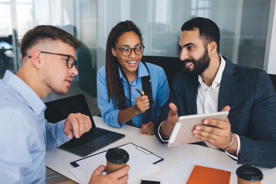 Smiling male and female experts browsing financial marketing information on exchange website using digital tablet in office interior, cheerful professionals enjoying brainstorming collaboration