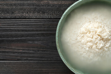 Bowl with rice soaked in water on black wooden table, top view. Space for text