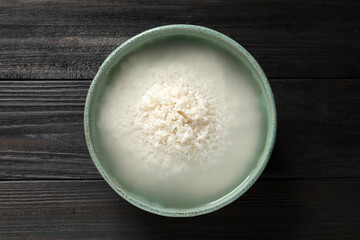 Bowl with rice soaked in water on black wooden table, top view