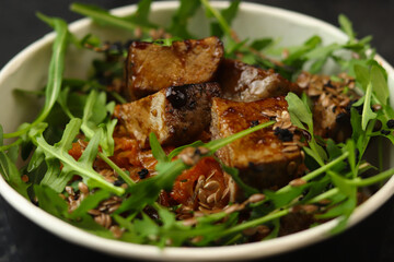 Close up of pieces of beef stewed in soy sauce with arugula in asian style on black background.