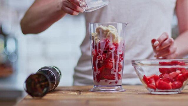 Woman making strawberry milk shake on kitchen table.