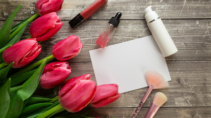 Feminine desk workspace with cosmetics, lipstick and tulip flowers on wooden background. Flat lay, top view