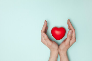 Health, medicine and charity concept - close up of female hands with small red heart