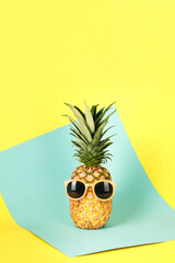 Pineapple dressed and sunglasses on a blue-yellow background. Vertical image.