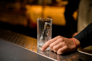 tall cocktail glass with piece of ice stand on bar counter.