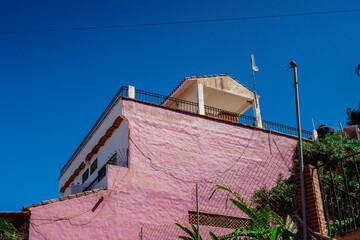 Beautiful pink traditional colonial Mexican building with wrought iron balcony and vibrant green palm tree out front