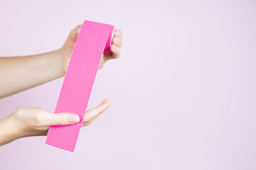  Woman holds in her hands a pink tape for lifting the skin of on pastel background. Kinesiotaping concept