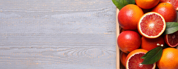 Ripe sicilian oranges with green leaves on grey wooden table, top view with space for text. Banner design