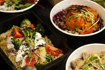 Lunch boxes with food ready for work or school, pre-cooking or diet on black background. Healthy food delivery service and daily ration concept.