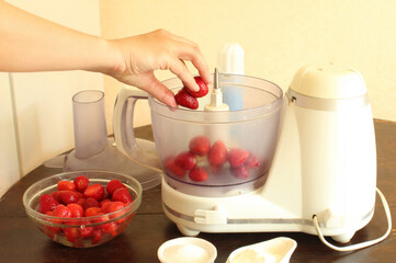 Close-up of a woman's hand pouring fresh strawberries into a food processor to make a strawberry milkshake. Make strawberry milkshake step by step. Summer strawberry cocktail