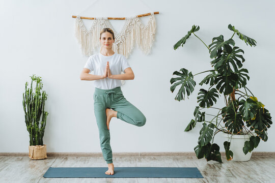 A young active girl stands on one leg with her arms connected. Practice yoga on the mat at home. Vrikshasana is a tree pose. Balance