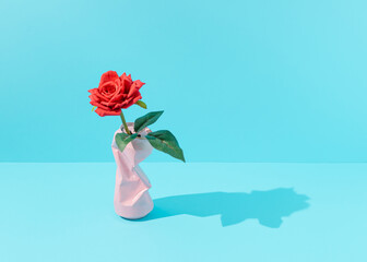 Red blossom rose flower in pastel pink colored crushed can against vibrant blue background. Minimal spring concept. Retro still life aesthetic.
