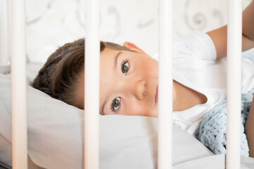 Adorable funny baby boy looking out the wooden bed.