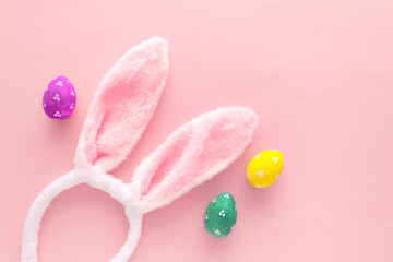 Decorated Easter eggs and bunny ears on color pink background, top view