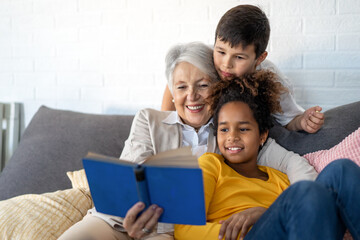 Happy grandmother, nanny helping to mixed race grandchildren with study. Homeschooling concept