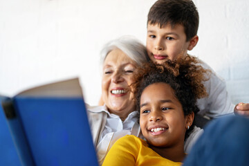 Happy grandmother, nanny helping to mixed race grandchildren with study. Homeschooling concept - obrazy, fototapety, plakaty