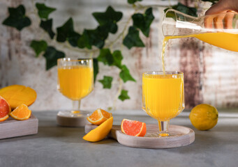 Glass of fresh orange juice with fresh fruit on a wooden table Still life with fresh orange juice in a glass with splashes and drops. The juice is pouring from the decanter into the glass