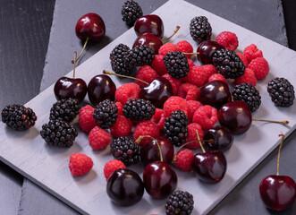 Cherries, raspberries and blackberries on grey stone board.