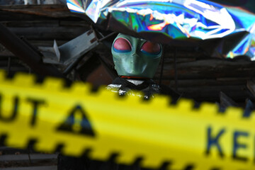 A close up image of a small green alien set up behind a yellow caution tape as a Halloween decoration. 