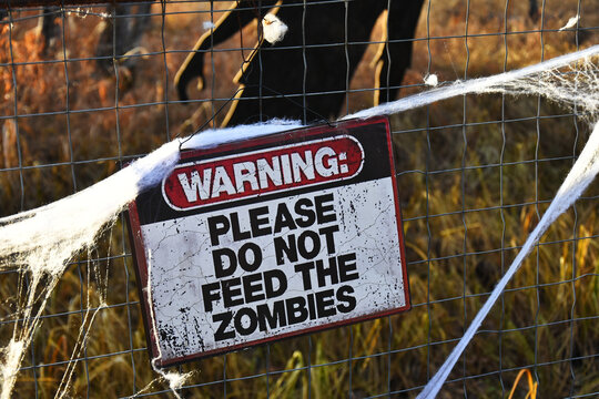 A close up image of a warning sign on a metal fence stating do not feed the zombies.