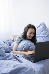 Happy young woman lying on bed with laptop.