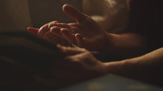 Crop senior husband and wife holding hands and flipping pages of photo album while recollecting old memories in weekend at home