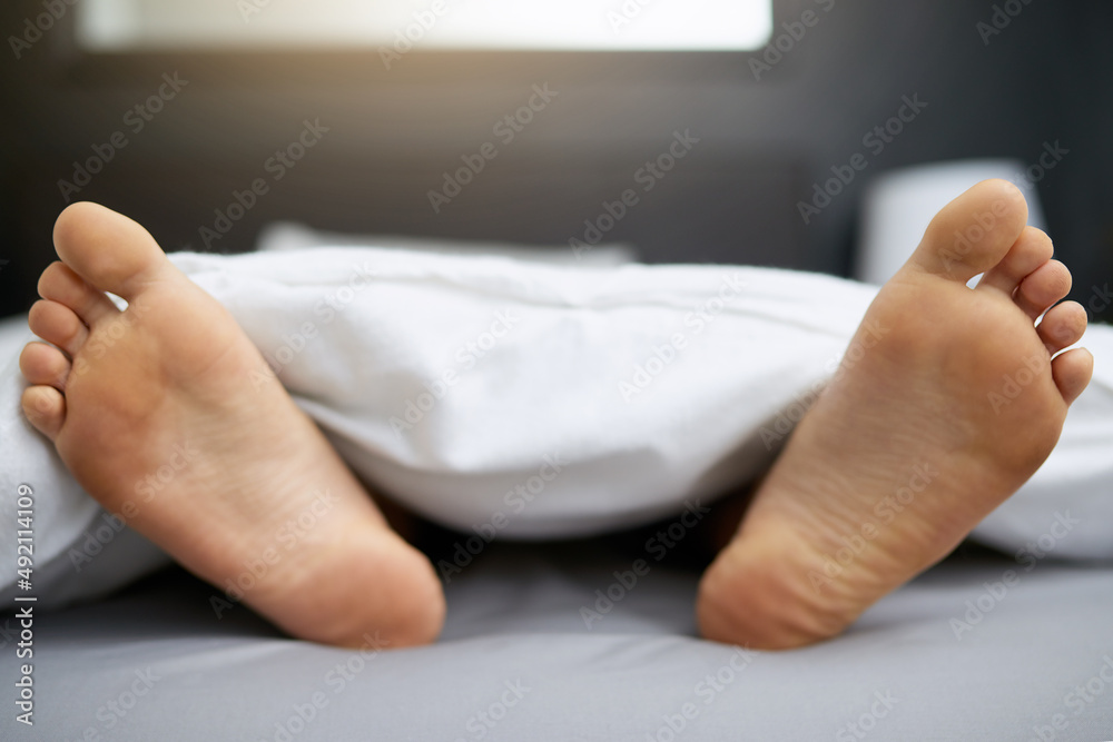 Wall mural Do not disturb. Shot of a young mans feet sticking out from underneath his duvet.