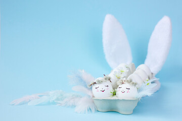 White Easter eggs with cute faces with feathers and bunny ears on blue background.