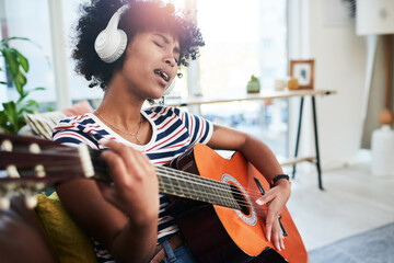 Music is a natural soother. Shot of a woman wearing headphones while playing the guitar at home.