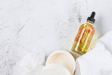 Spa and beauty. A bottle of natural oil with flower buds, a white jar of cream and a white terry towel are on a gray background. Copy space. View from above.