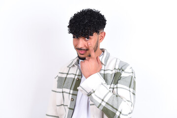 young arab man with curly hair wearing overshirt over white background, looking, observing, keeping an eye on an object in front, or watching out for something.