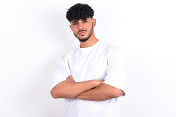 Waist up shot of  self confident young arab man with curly hair wearing white t-shirt over white...