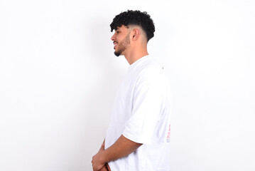 Profile of smiling young arab man with curly hair wearing white t-shirt over white background  with healthy skin, has contemplative expression, ready to have outdoor walk.