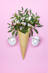 Easter eggs and waffle cone with spring flowers on pink background.
