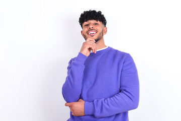 Fototapeta na wymiar young arab man with curly hair wearing purple sweatshirt over white background laughs happily keeps hand on chin expresses positive emotions smiles broadly has carefree expression