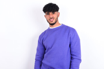 Portrait of dissatisfied young arab man with curly hair wearing purple sweatshirt over white wall...