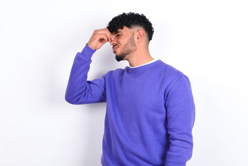 Sad young arab man with curly hair wearing purple sweatshirt over white background suffering from headache holding hand on her face